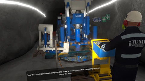 Worker at a control station beside a blue raise boring machine inside a mine tunnel.